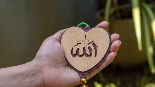 Free Person holding a heart-shaped wooden piece with Islamic calligraphy outdoors. Stock Photo