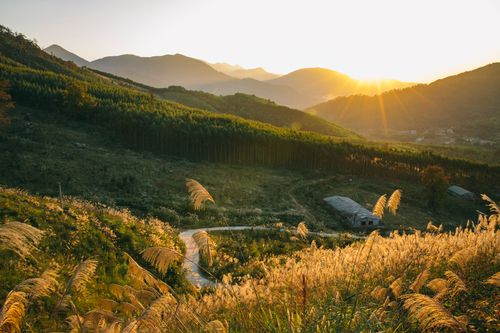 Free A breathtaking sunset illuminates a rural valley with mountains and lush fields, creating a tranquil scene. Stock Photo