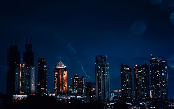 A dramatic night view of the Jakarta skyline illuminated by lightning, showcasing the city's vibrant architecture.