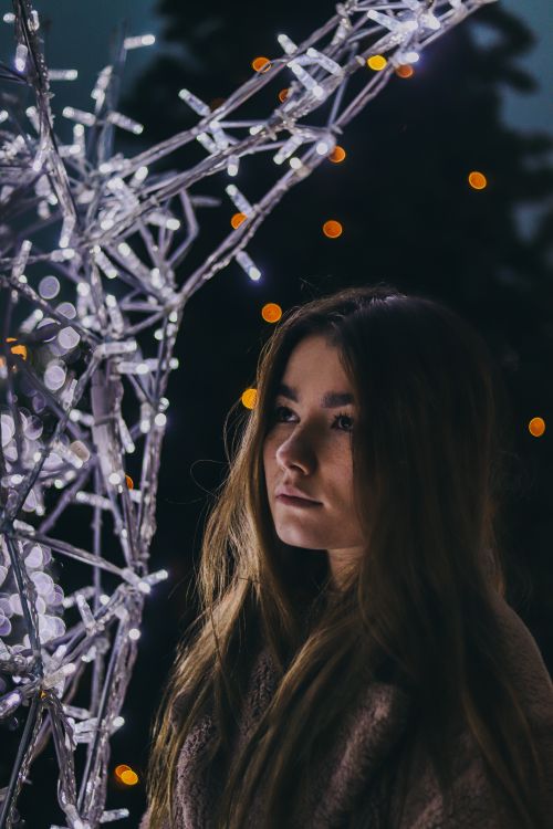 Free Portrait of a woman with long hair gazing at an illuminated sculpture with bokeh lights in the background. Stock Photo