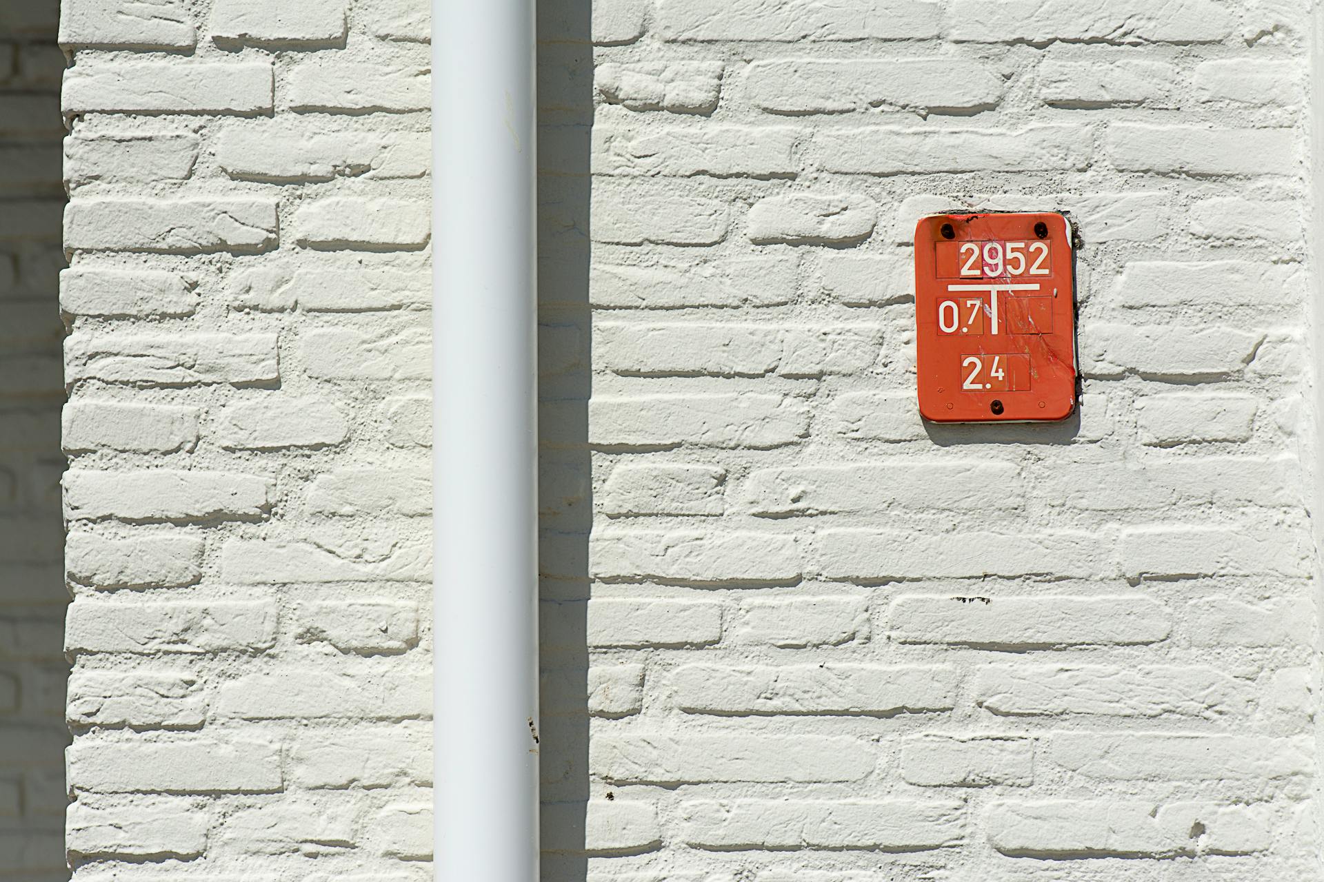 Close-up of a white brick wall featuring a red numbered sign with a white gutter pipe.