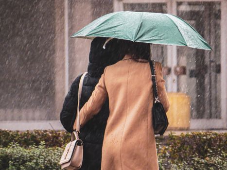 Two people walking closely under an umbrella on a snowy city day.