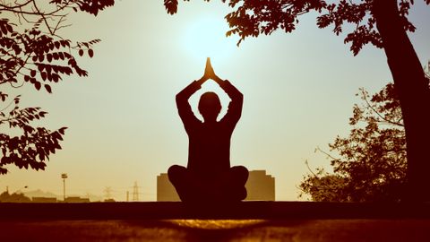 Silhouette of a person practicing yoga outdoors during sunrise, creating a calming atmosphere.