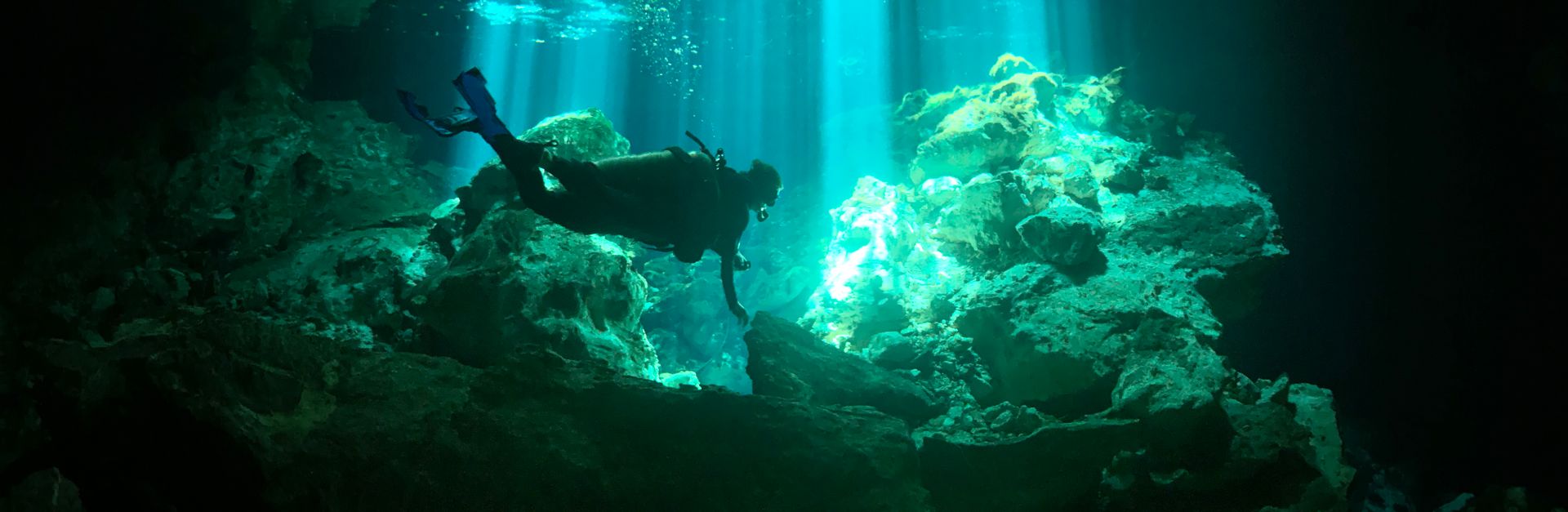Scuba diver explores serene underwater coral formations illuminated by natural light rays.