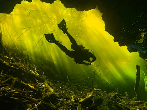 A Diver Swimming Underwater Near a Cave