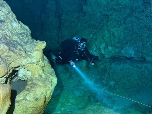 Underwater Photography of a Person in Black Scuba Suit Swimming Through the Caves