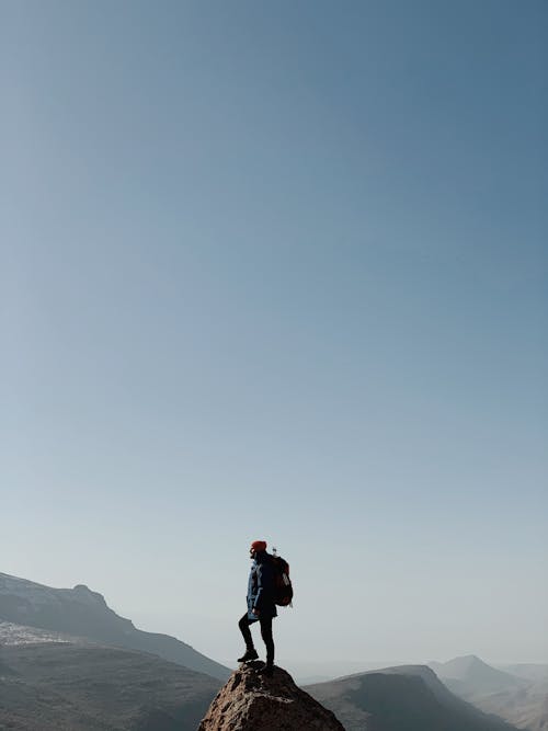 A Man Standing on Top of the Rock Formation Under the Blue Sky