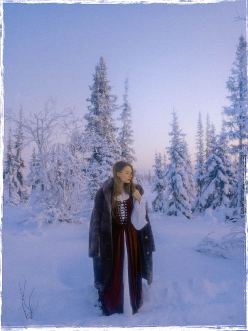 A woman in traditional attire stands in a snow-covered forest, evoking winter serenity.