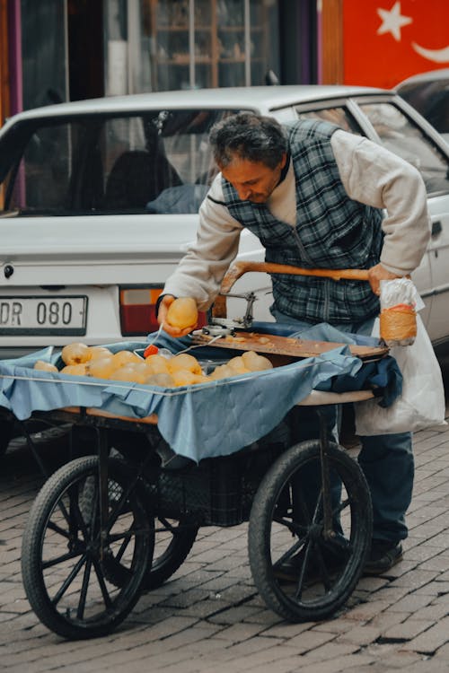 A Man Standing Beside a Cart Holding a Fruit