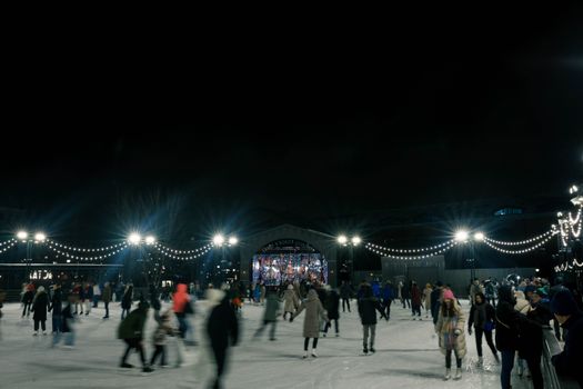 People enjoy ice skating under lights on a winter night.