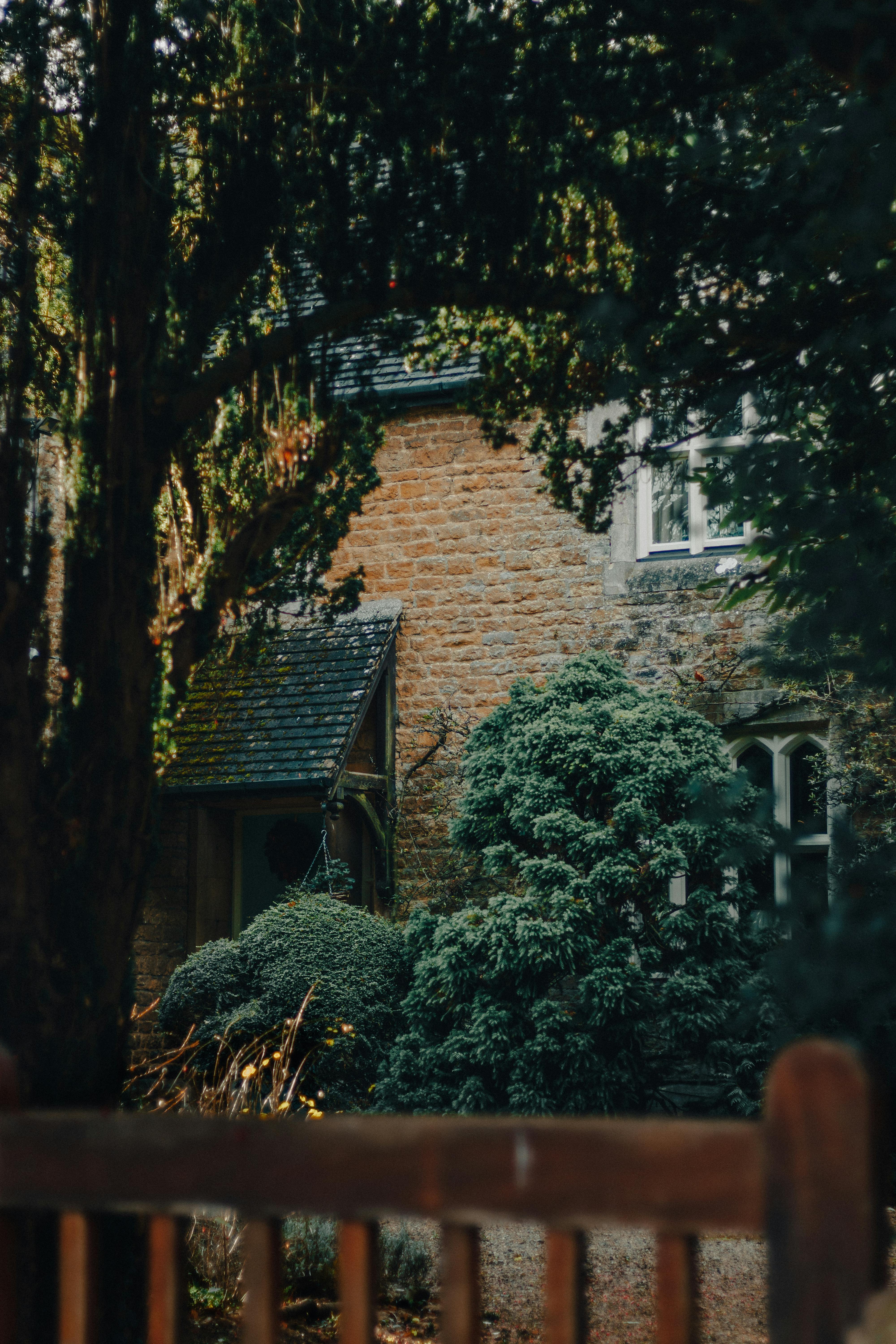 Tranquil scene of a rustic brick cottage nestled amidst lush greenery and trees.
