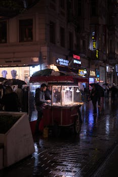 A bustling evening scene with a street food stall and people walking in the rain.