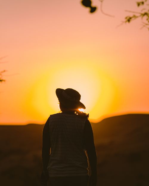 Free A person in a hat gazes at a vibrant sunset in the UAE desert. Stock Photo