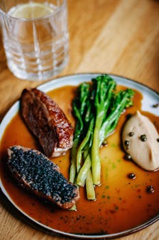 Close-up of a gourmet dish with meat, asparagus, sauce and a glass of lemonade.