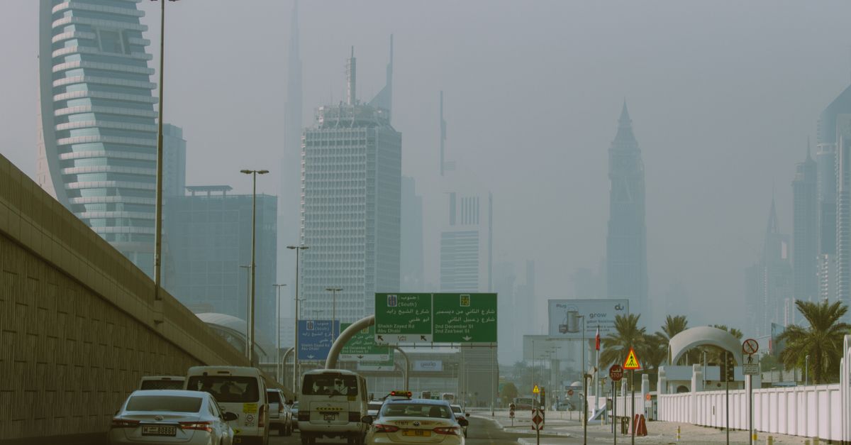 A police patrol vehicle stands parked along a multi-lane Dubai highway as high-speed cars drive past skyscrapers.