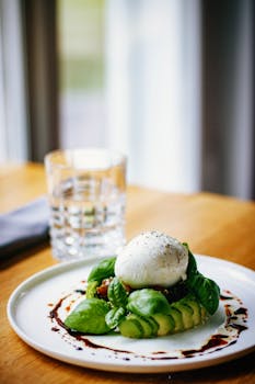 Delicious plate of mozzarella and avocado salad with a glass of water on a wooden table.