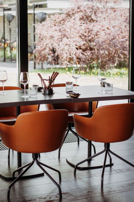 A modern restaurant interior with stylish chairs, table set with glasses against a window view of a garden.