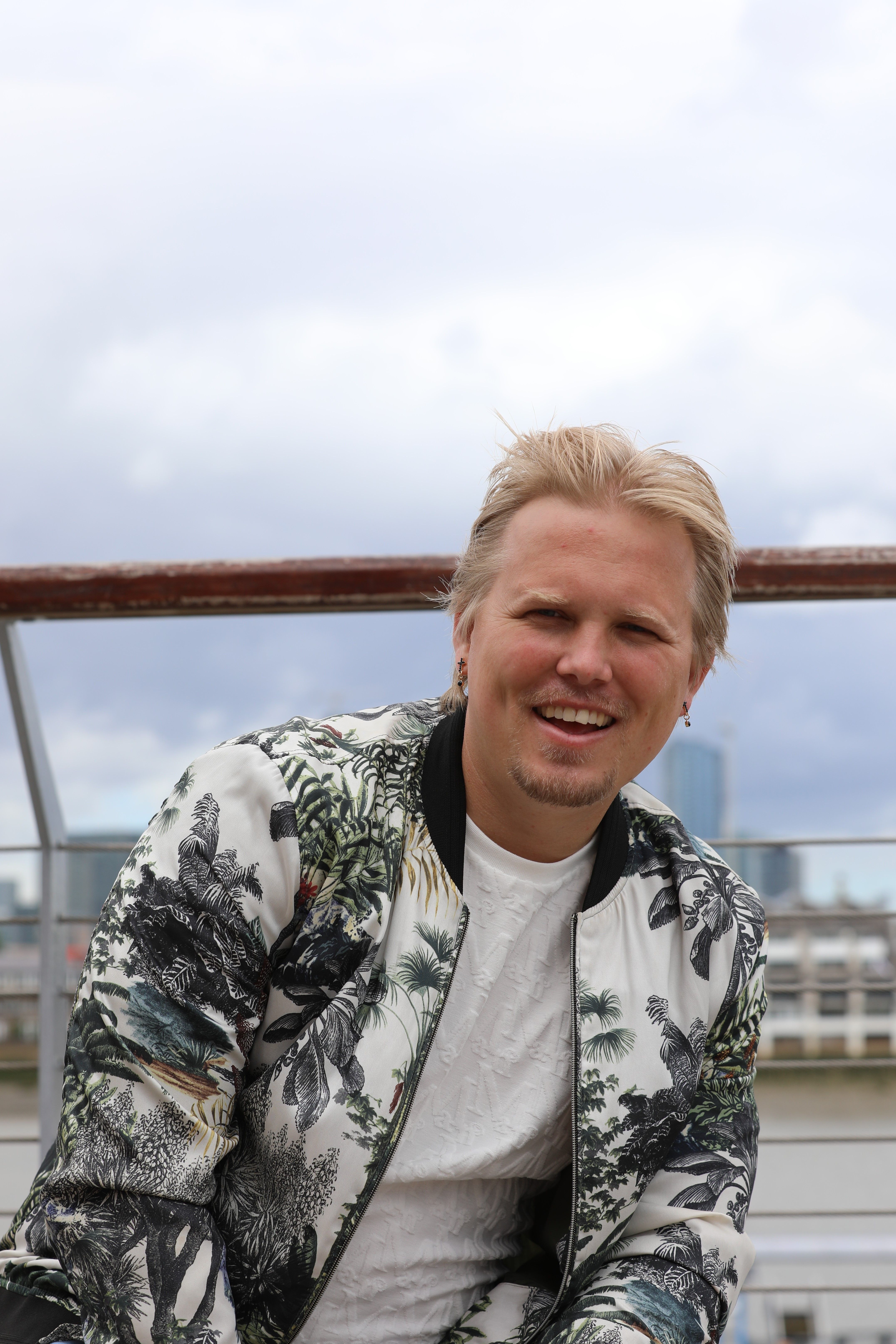 Person smiling wearing a floral jacket on a London terrace with city view.