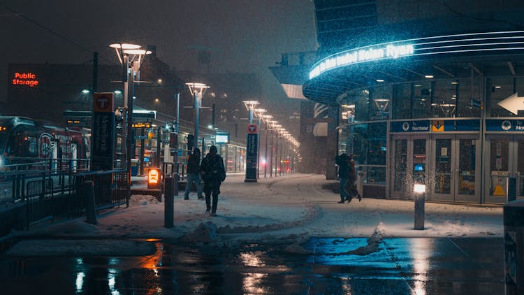 People Walking On Snow Covered Sidewalk At Night