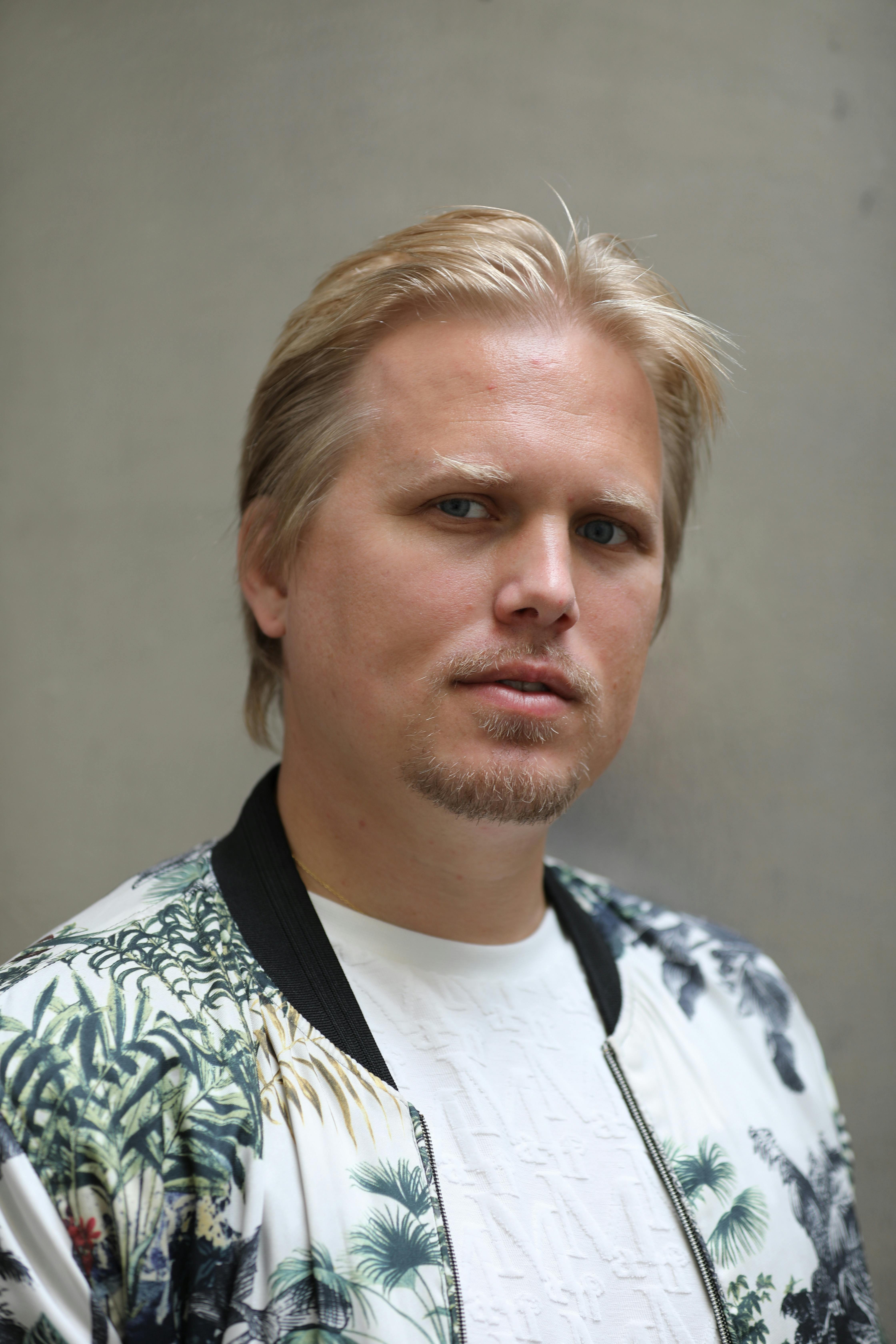 Close-up portrait of a man in a floral jacket against a neutral background.