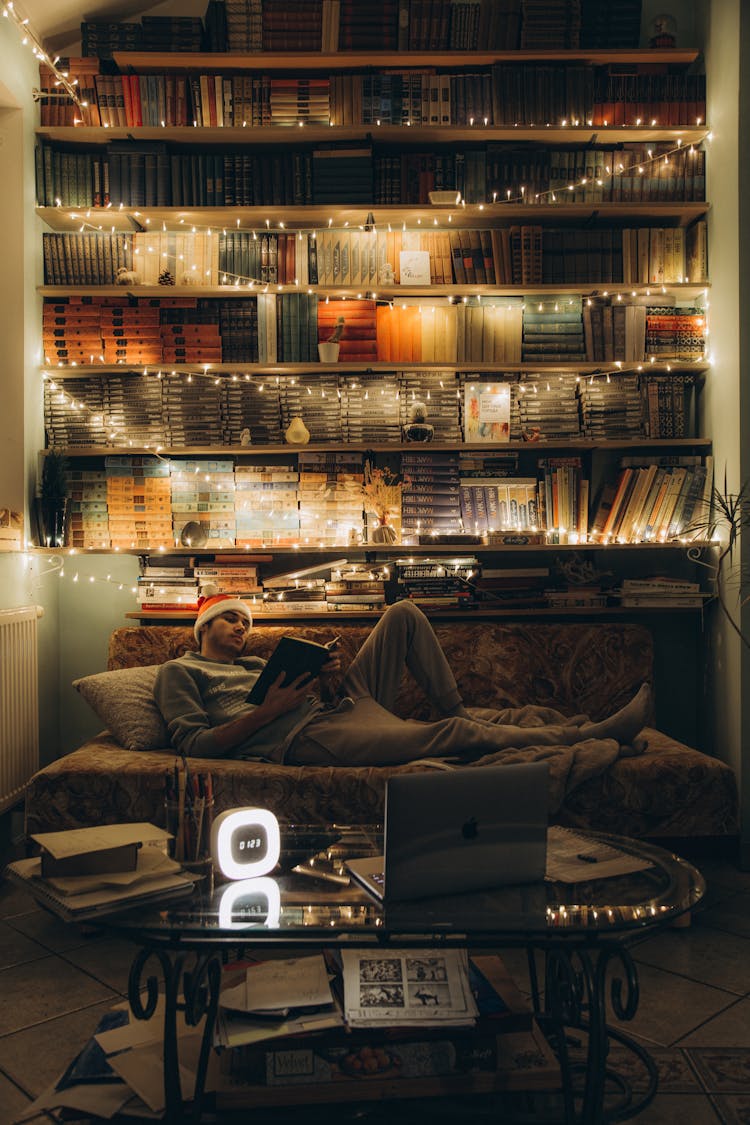 Man In Sweatpants Lying On A Sofa In Front Of A Bookshelf