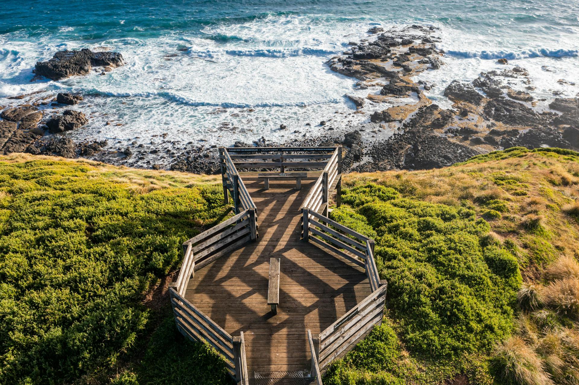 A stunning aerial view of a boardwalk overlooking Phillip Island's rugged coastline and ocean waves.