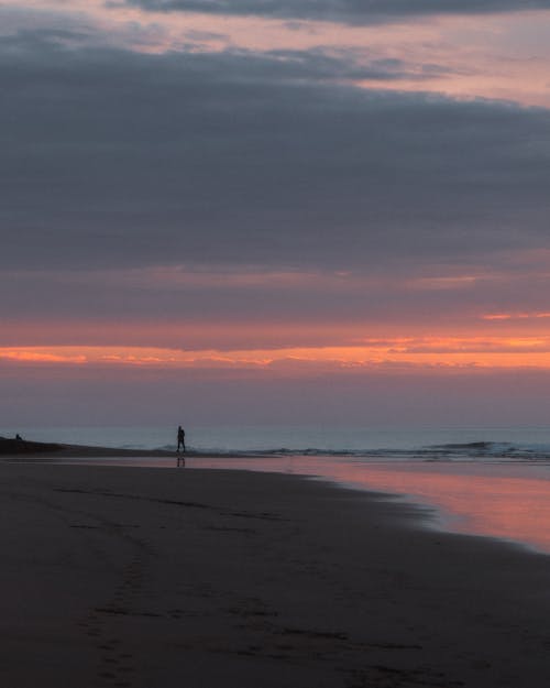 Person Walking on Beach during Sunset