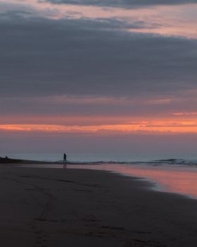 A person walks along Anglesea beach during a vibrant sunset, capturing a peaceful moment.