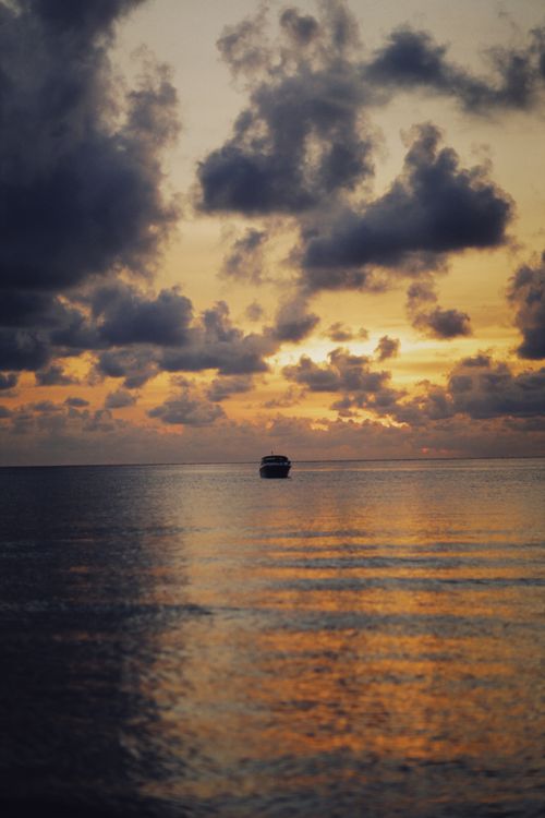 Free A tranquil scene of a boat sailing at sunset with a cloudy sky reflecting on the water. Stock Photo
