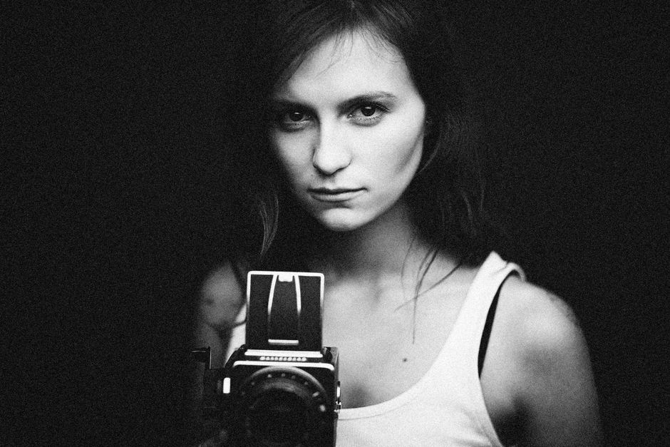 Black and white portrait of a woman holding a vintage camera, conveying classic elegance.