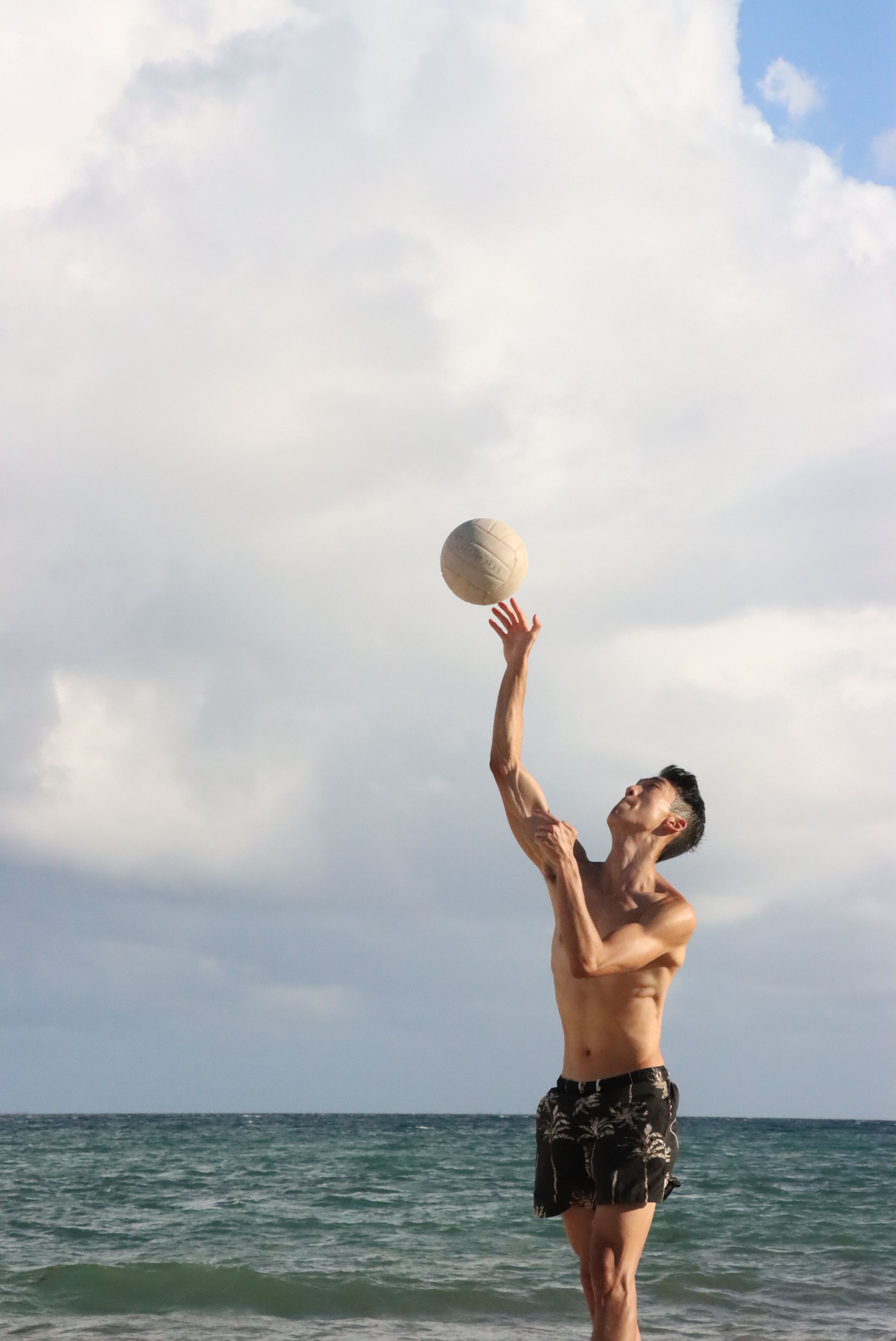 Shirtless man enjoying a game of toss on a sunny beach with clear skies.