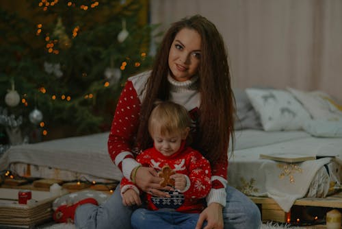 Free A Woman in Ugly Christmas Sweater Sitting Near Her Son Holding a Cookie Stock Photo