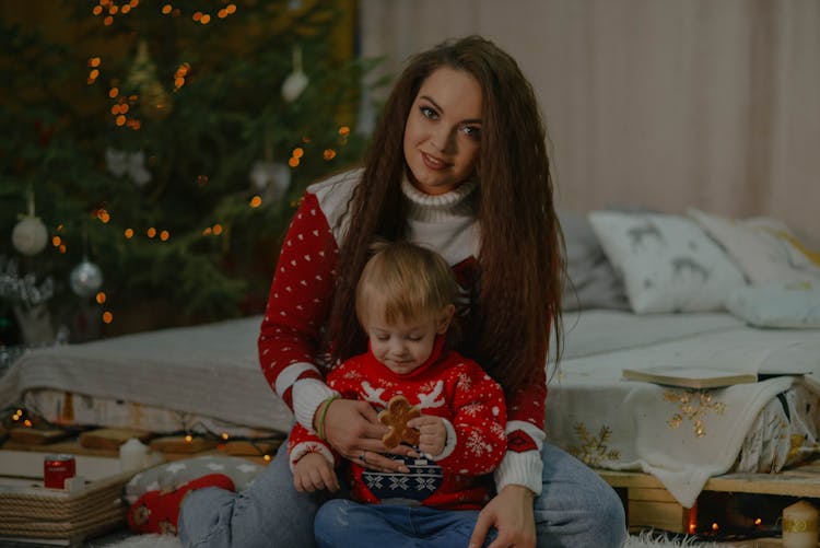 A Woman In Ugly Christmas Sweater Sitting Near Her Son Holding A Cookie