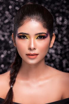 Close-up portrait of a woman with vibrant makeup and braided hair against a bokeh background.