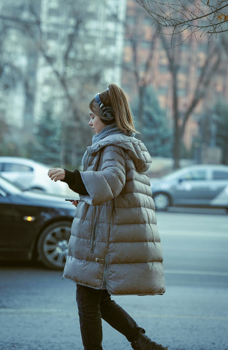 A Woman In Puffer Jacket Walking On The Street While Wearing Headphones
