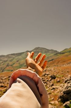 A hand reaching towards a scenic mountain landscape in Turkey under a clear sky.