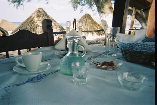 A rustic outdoor dining table with a coffee cup and glassware, overlooking a beach setting.