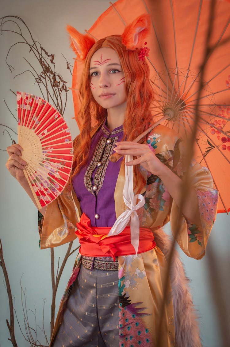 A Woman Wearing A Costume Holding An Umbrella And A Hand Fan