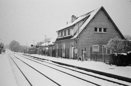 Free A Grayscale Photo of Houses on a Snow Covered Ground Near the Railroad Stock Photo