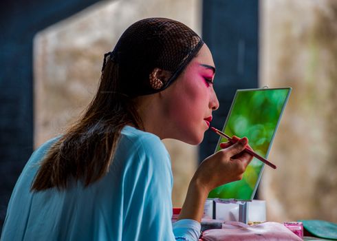A woman carefully applying lipstick, reflecting artfully in a mirror with a blurred background.