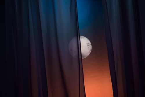 Free A full moon gently glows through parted dark curtains, creating a mystical night sky ambiance. Stock Photo