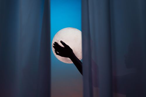 Free Silhouette hands framed between curtains, reaching for a bright full moon in the night sky. Stock Photo