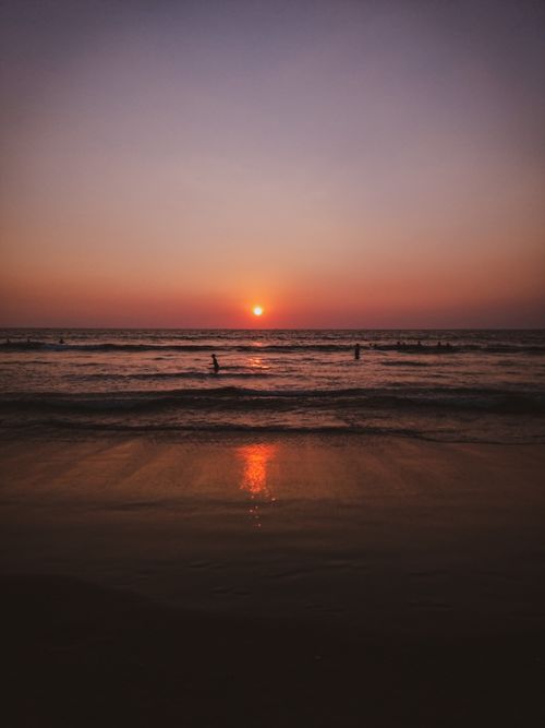 Free Peaceful evening at the beach with the sun setting over the ocean and silhouettes of people. Stock Photo