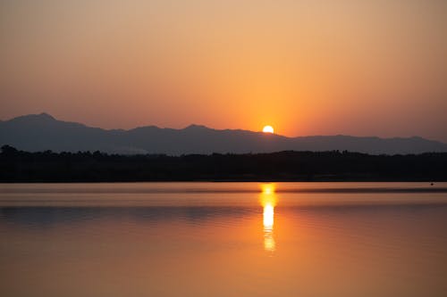 A Sun Setting Over a Mountain Near a Lake