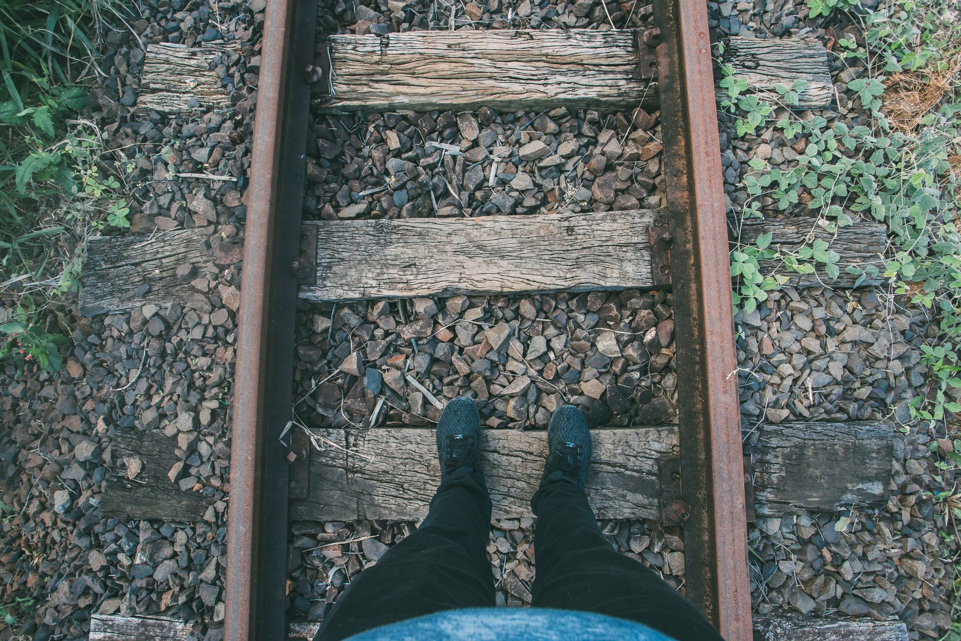 Person standing on rustic railway tracks with rocky surroundings.