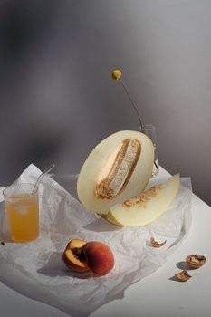 Artistic still life with melon, peach, and juice on paper-wrapped table.
