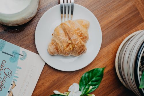 Free Top-down view of a fresh croissant on a plate, styled with a book and plant for an inviting breakfast scene. Stock Photo