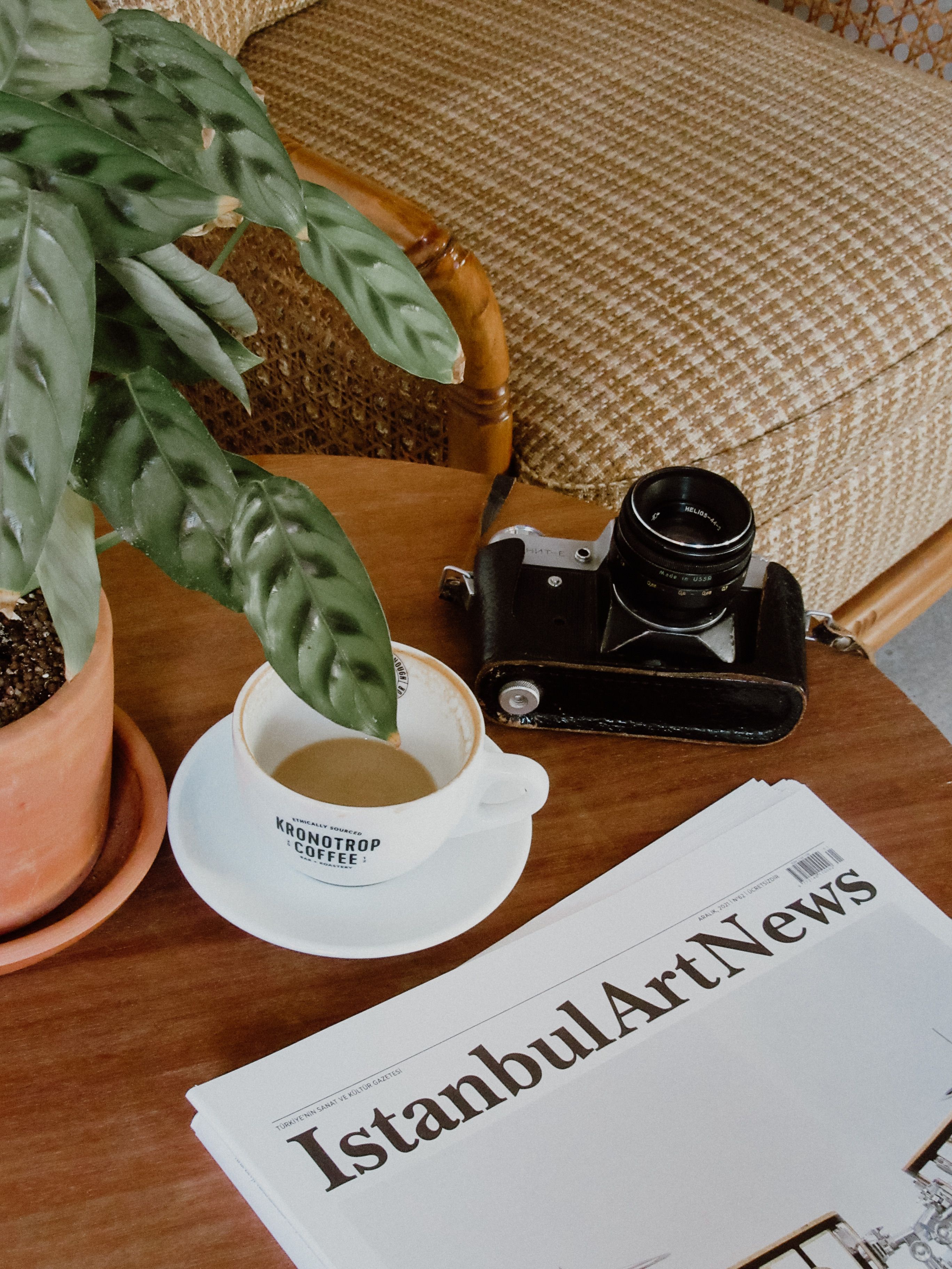 A vintage camera beside coffee and newspaper in a cozy Istanbul café setting.