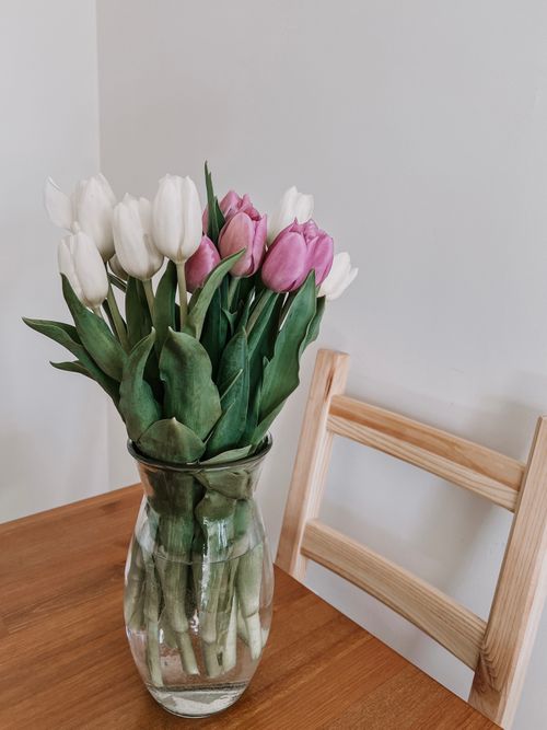 Free A beautiful arrangement of white and pink tulips in a glass vase on a wooden table, creating a delicate and fresh atmosphere. Stock Photo