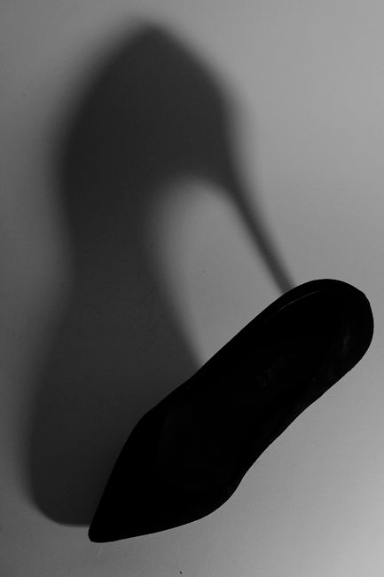 Fotomural Foto en blanco y negro de un zapato de tacón negro proyectando una sombra impactante sobre un fondo plano.